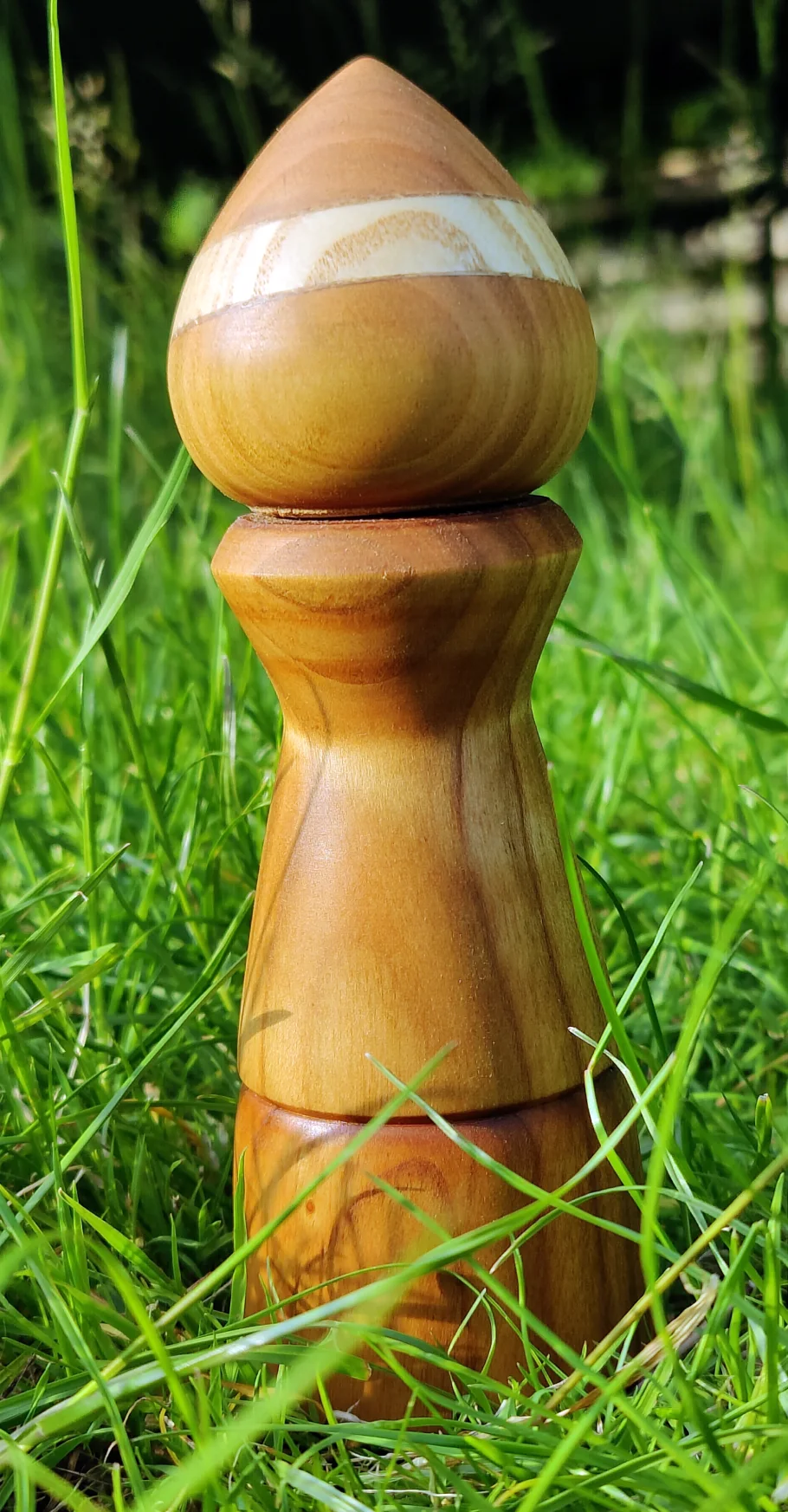small pepper grinder made from cherry standing on a lawn