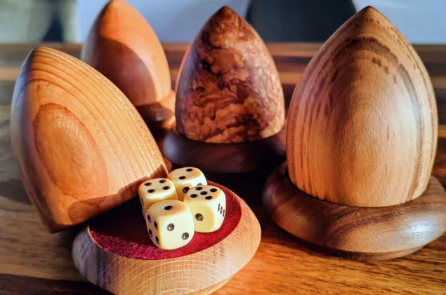 4 raffle cups. the one in front has it's lid leaning on the base revealing 4 dice on red felt